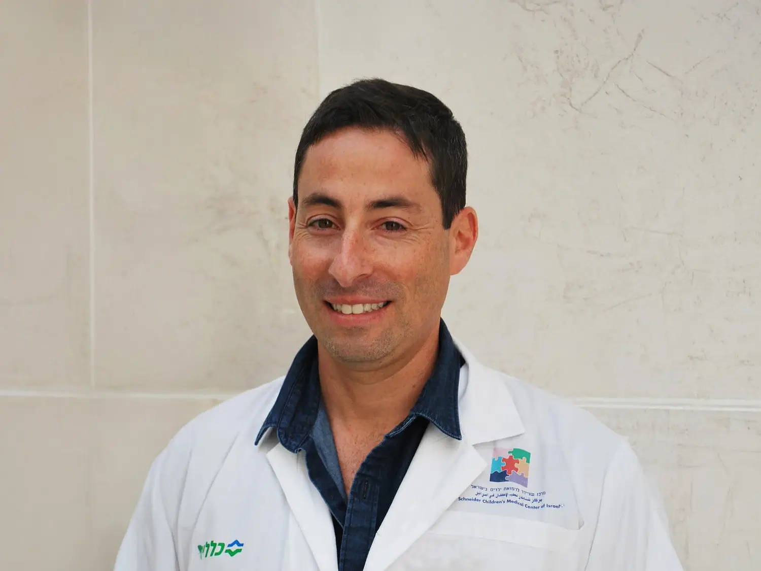 Dr. Amir Kershenovich smiling in a white coat with the Schneider Children’s Medical Center logo