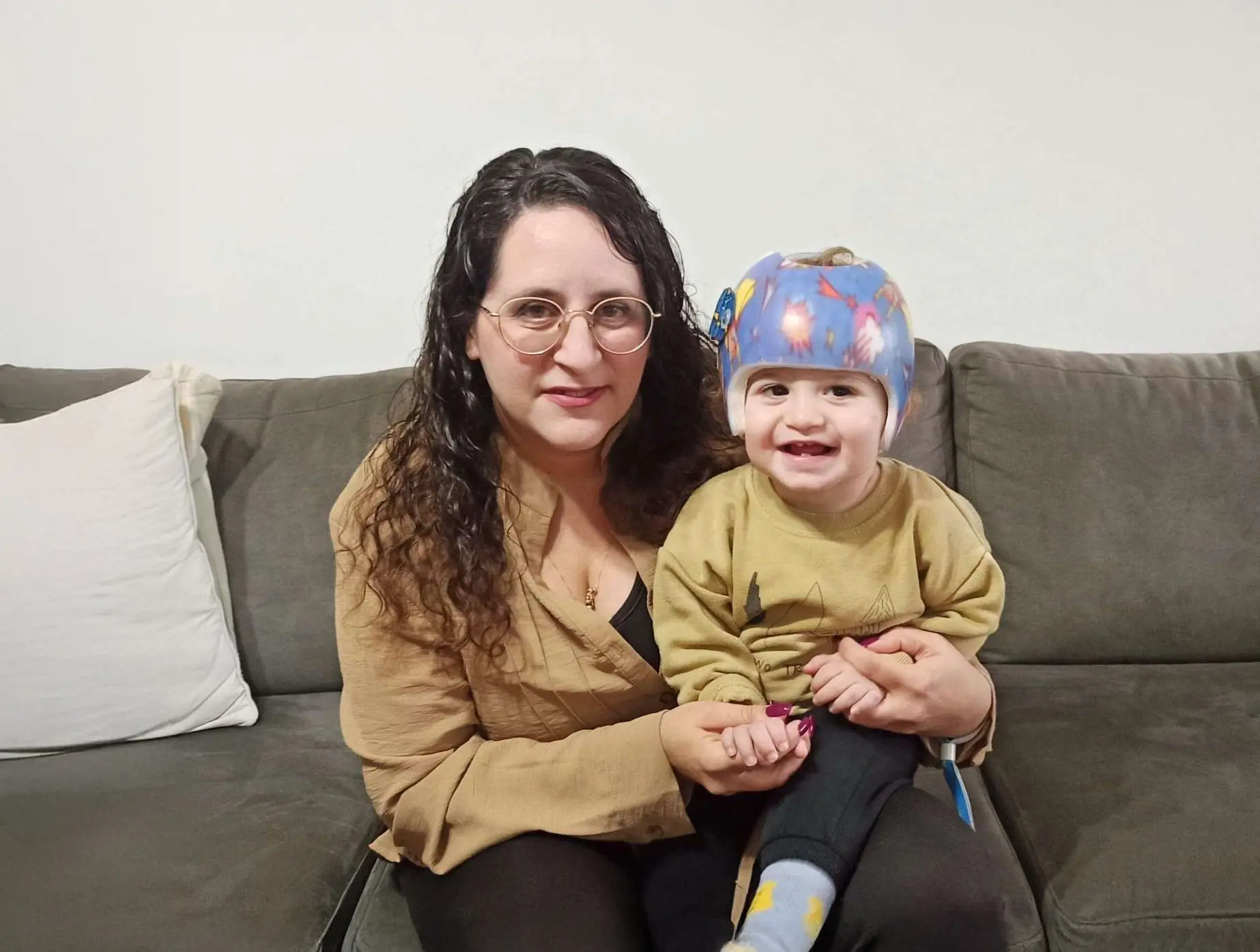 Smiling mother holding baby wearing a cranial helmet for plagiocephaly
