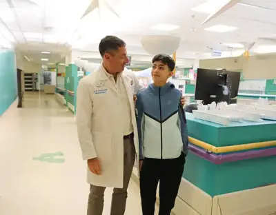 Dr. Amir Kershenovich standing with a teenage patient, smiling together at the hospital corridor after treatment
