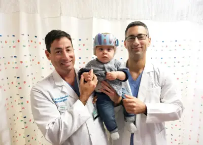 Dr. Amir Kershenovich and a colleague holding a baby wearing a cranial helmet after treatment for plagiocephaly